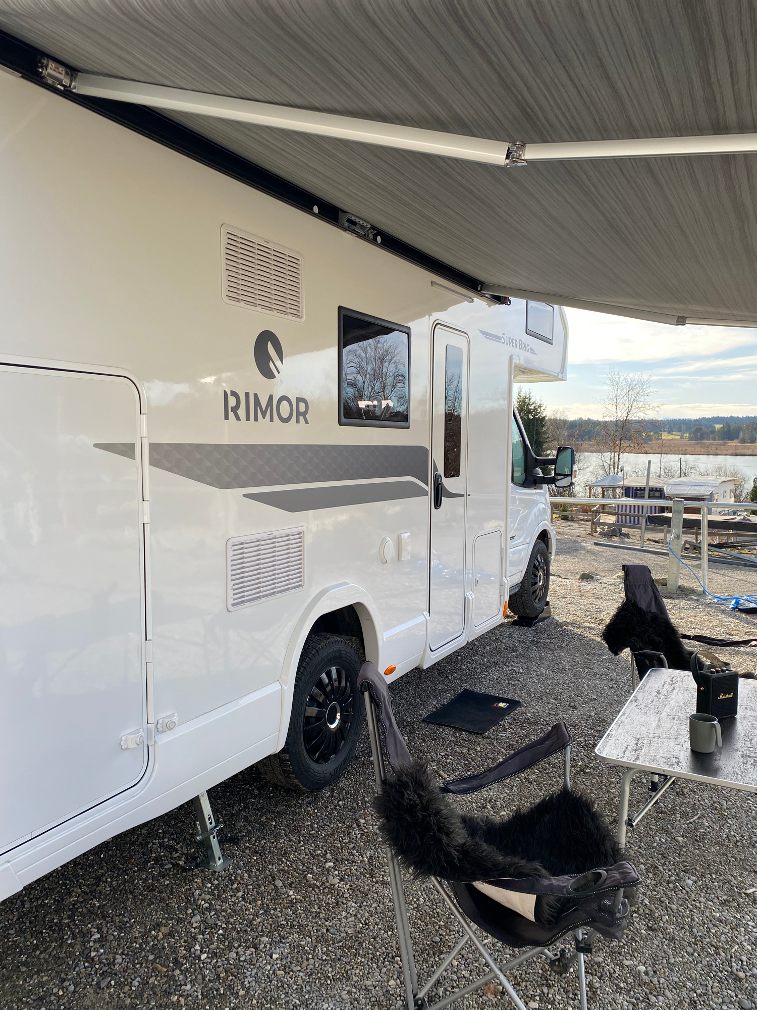 Seitenansicht unter der großen Markise Weißer Wohnmobil mit Markise und Campingstuhl im Freien.