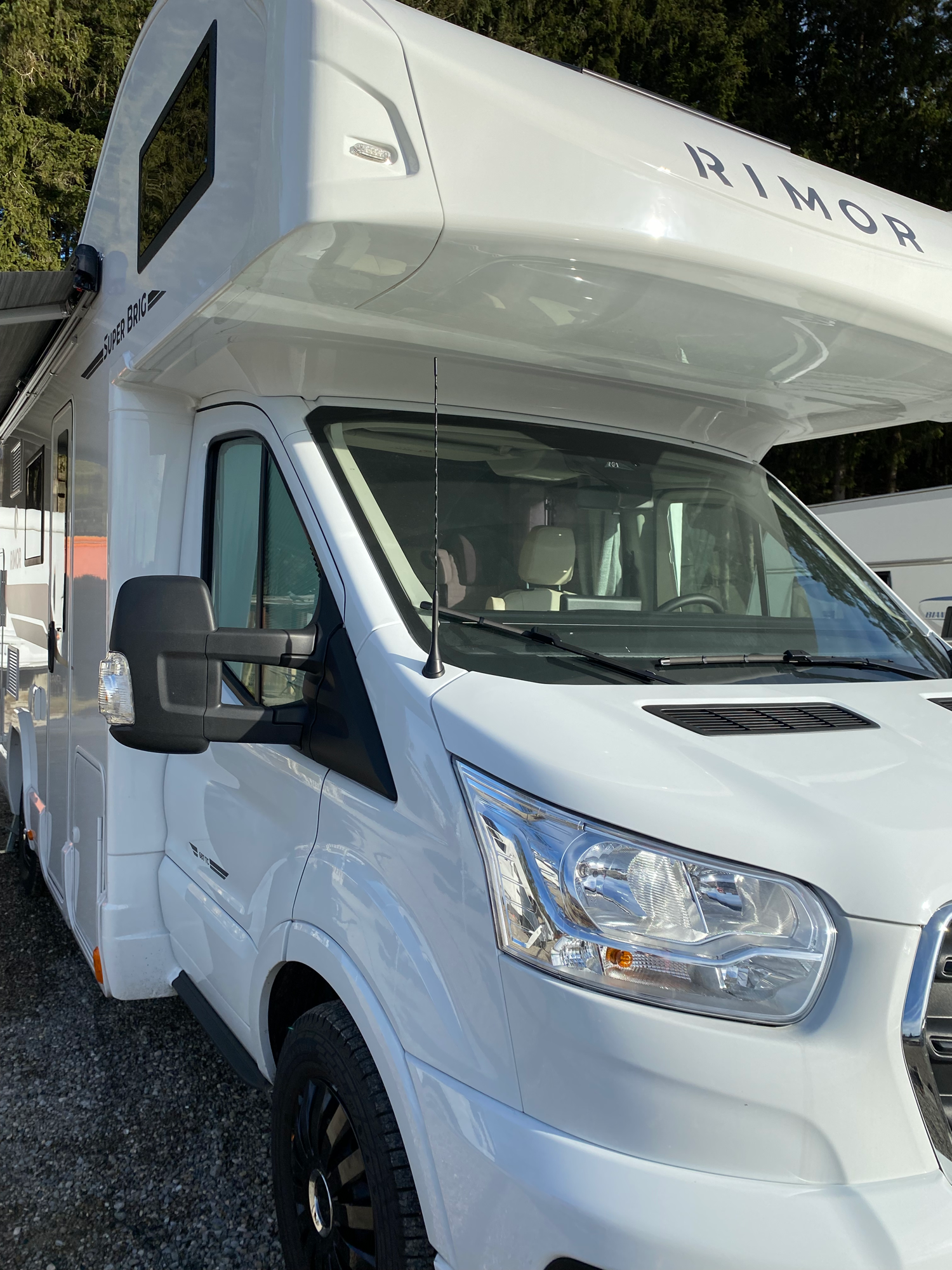 Front inkl. der Alkove mit Fenstern Weißer Wohnmobil mit Hochdach, geparkt in einer ländlichen Umgebung.
