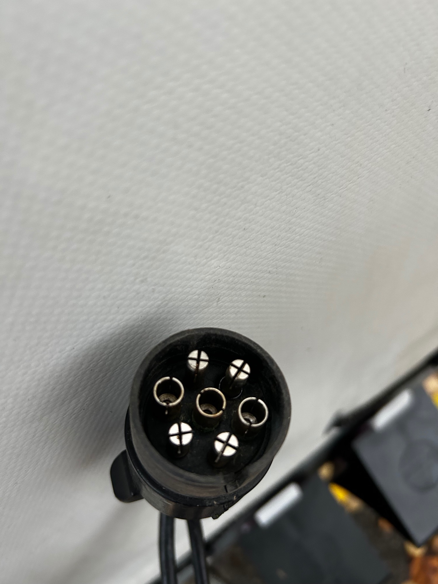 Stecker Rundstecker mit vier goldenen Pins, auf grauem Hintergrund.