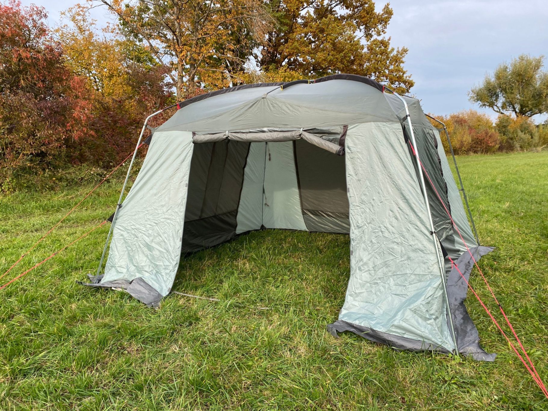 Pavillon High Peak Siesta Zelt mit offenen Eingängen, auf einer grünen Wiese, umgeben von buntem Laub.
