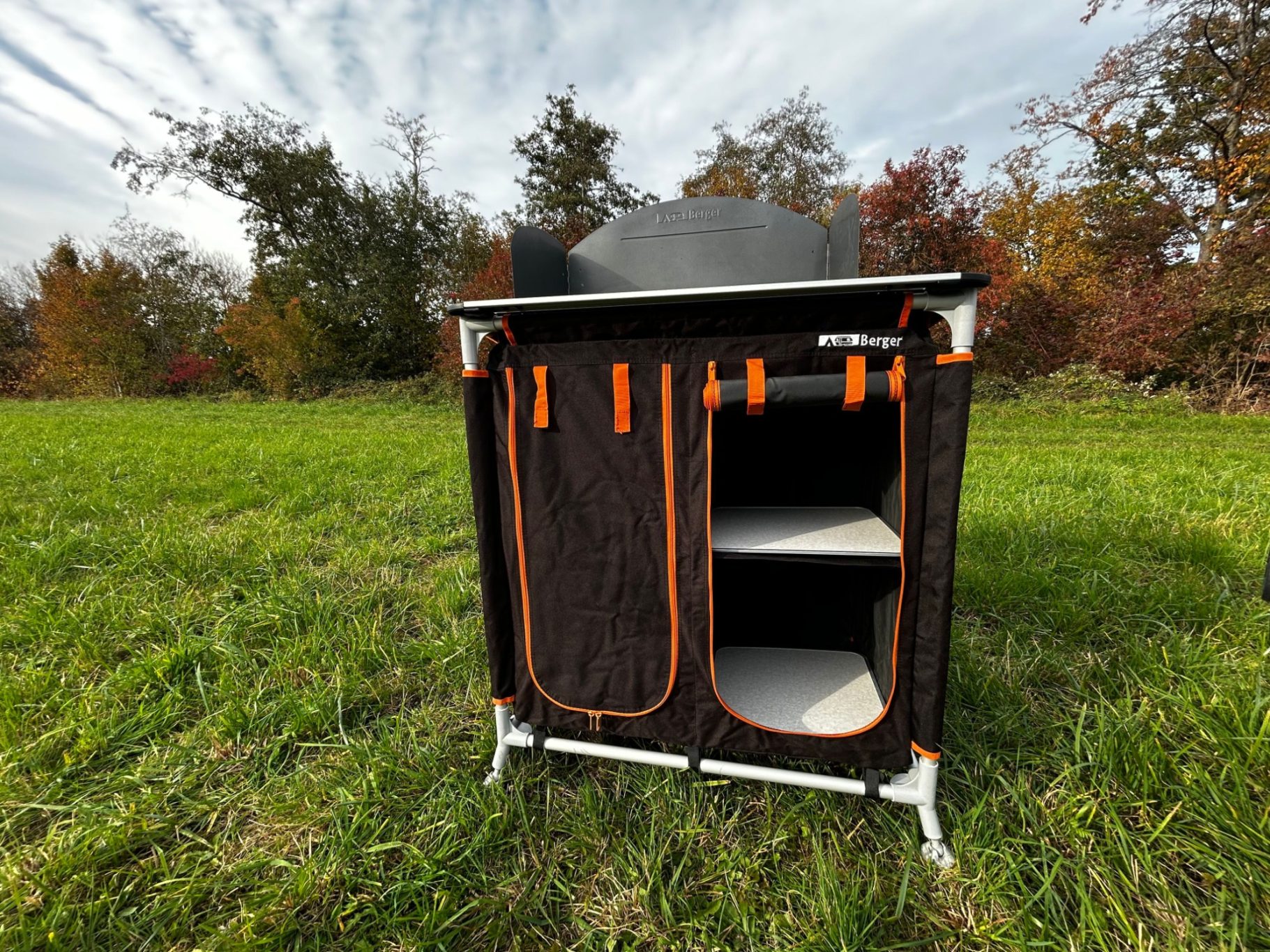 Fritz Berger Campingküche Schwarzer Camping-Schrank mit zwei Regalen und orangefarbenen Akzenten im Freien.