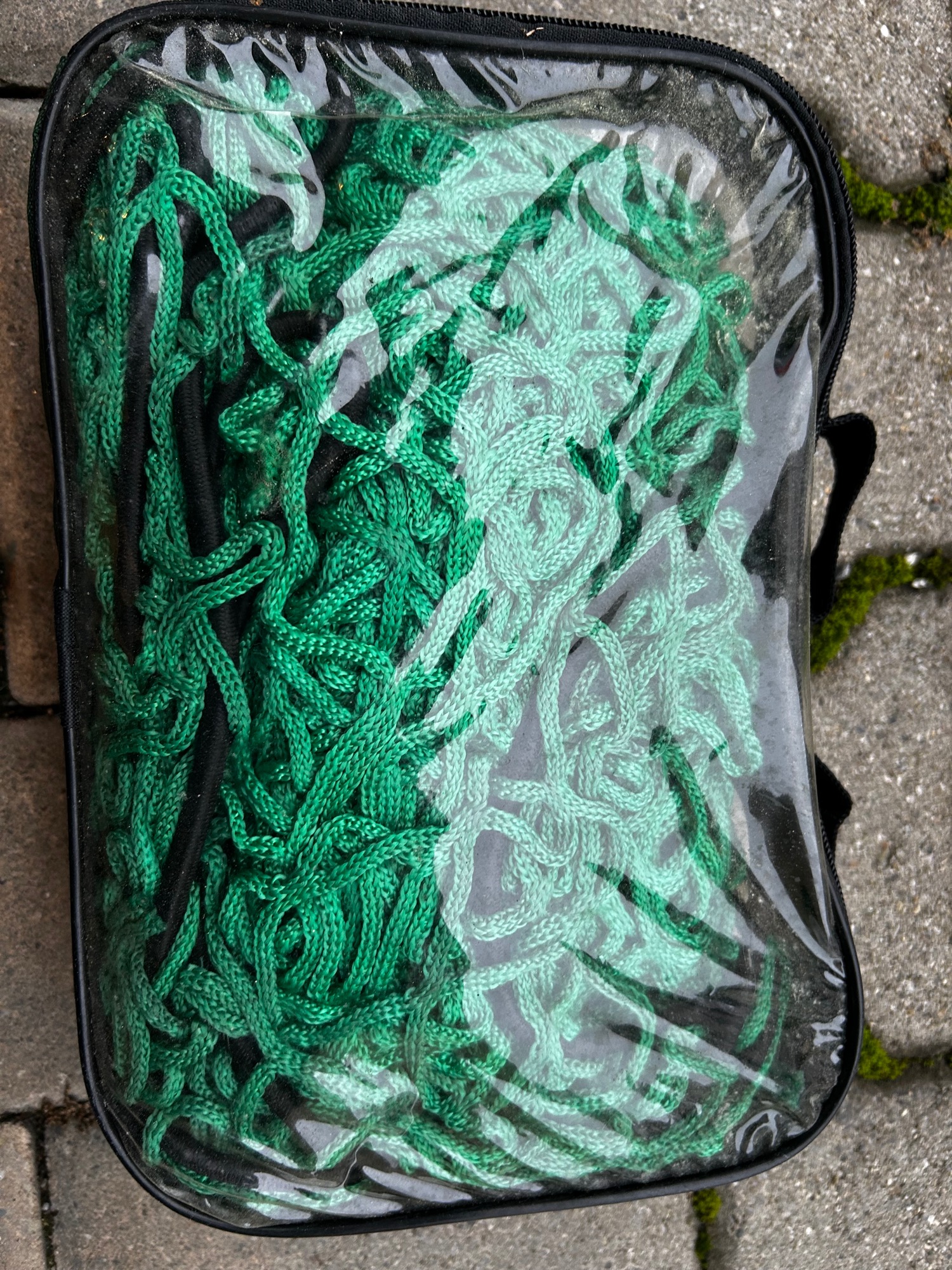 Transportnetz Grüne Schnur in transparentem Beutel auf einem Pflastersteingrund.