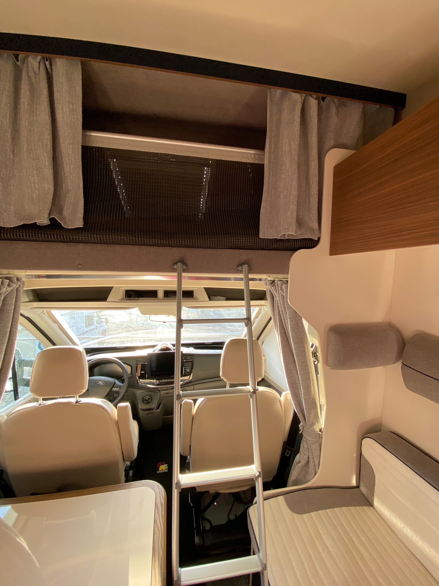 Zugang zur Alkoven, die mit Vorhängen abgetrennt werden können Wohnmobil-Interieur mit Sitzgruppe, Leiter und Stauraum über dem Fahrersitz.