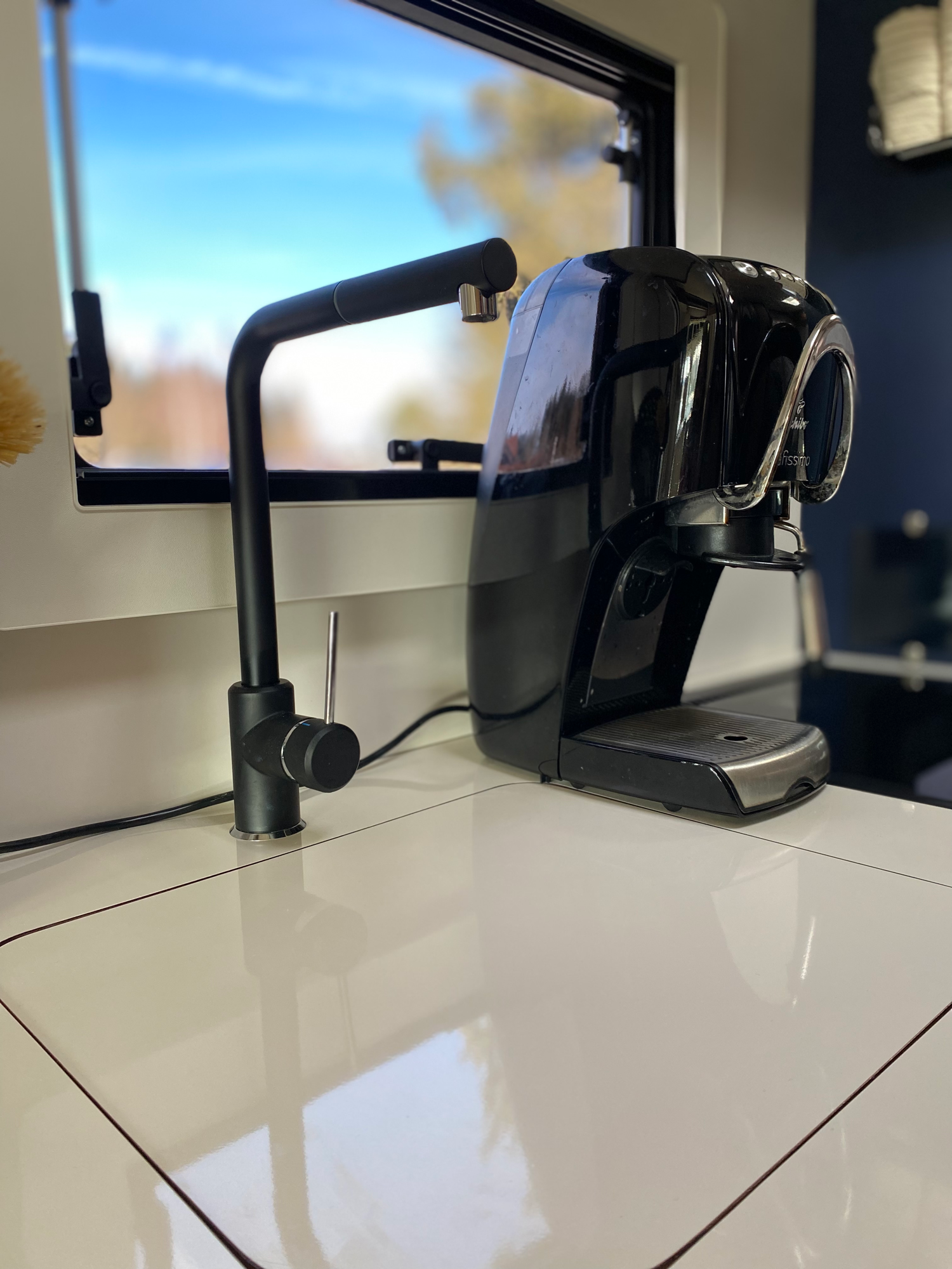 Eine Cafissimo ist ebenfalls an Board Schwarz glänzender Wasserkocher auf einer weißen Küchenzeile mit Fenster im Hintergrund.