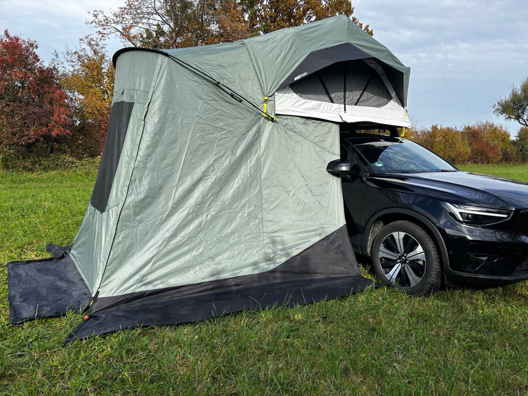 Vorzelt geschlossen Zelt in einem grünen Farbton, angebaut an der Seite eines schwarzen Autos auf einer Wiese.