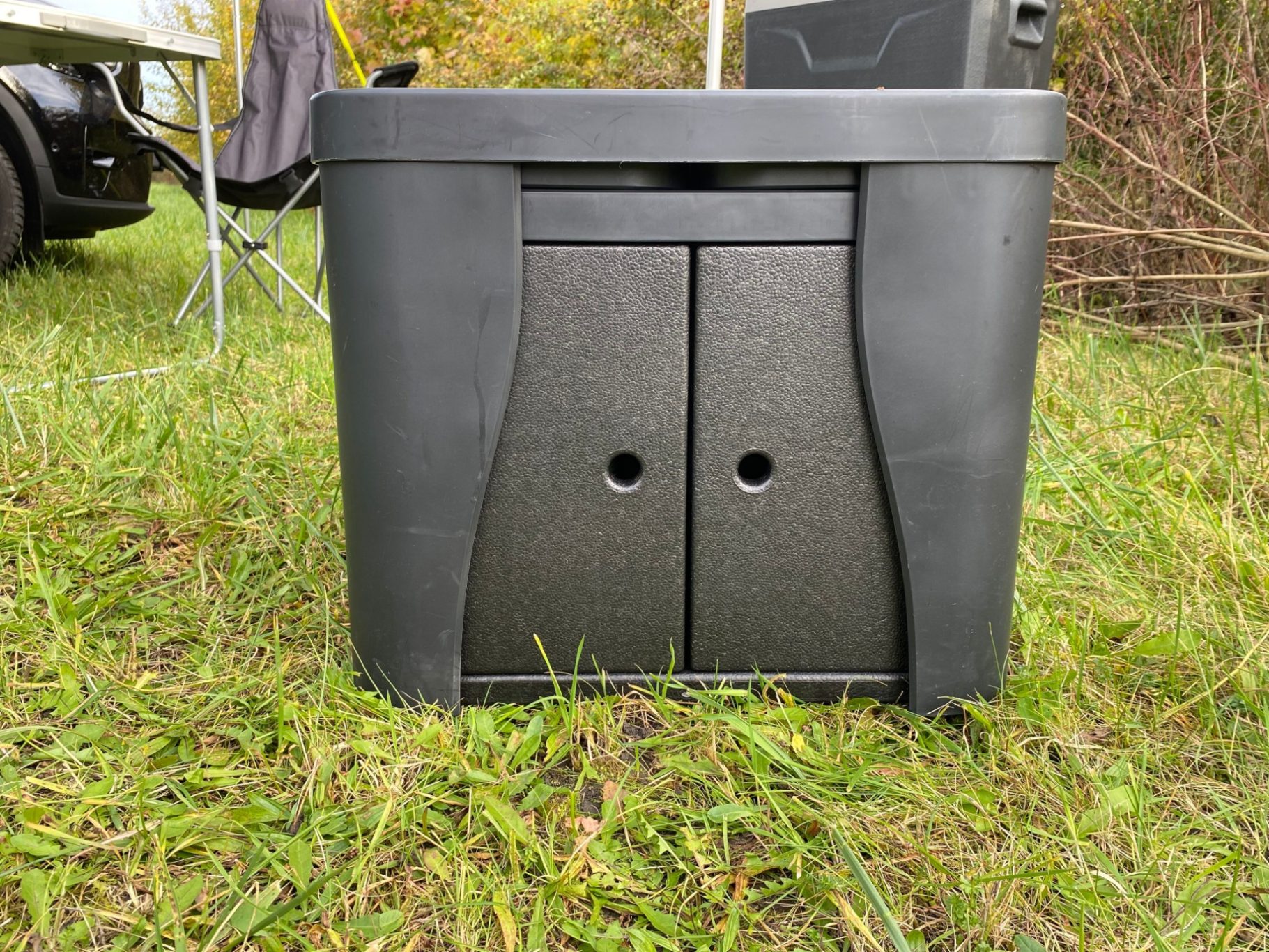 Outdoorküche transportfertig Schwarzer, quadratischer Aufbewahrungskasten mit Türen und Löchern, auf Gras plaziert.