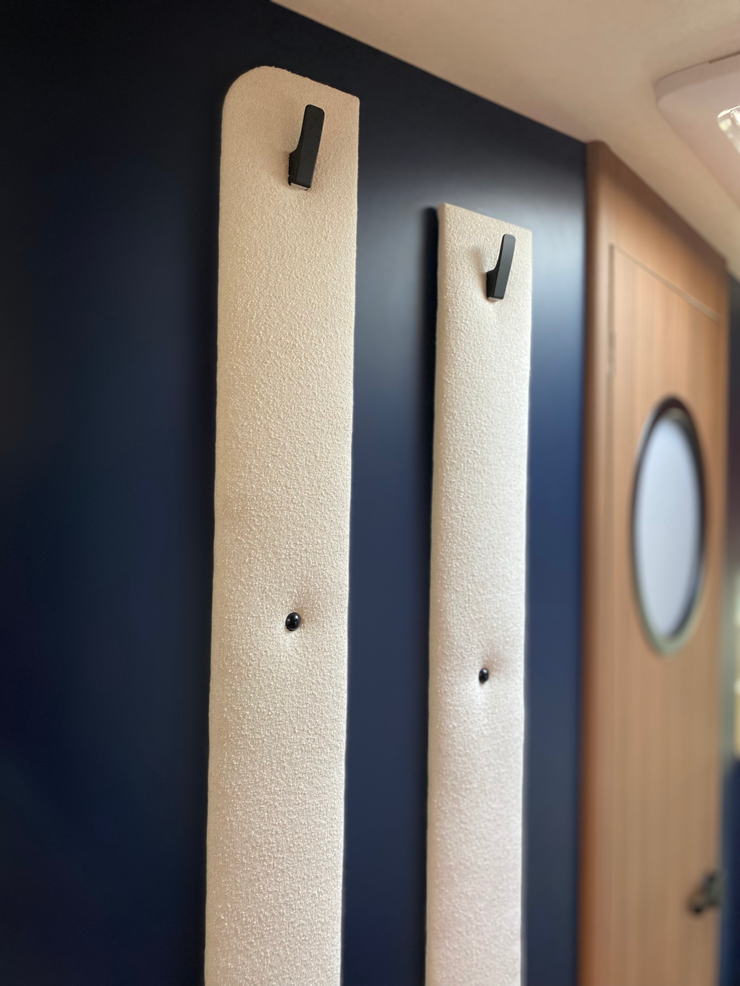 Garderobe neben dem Kleiderschrank Zwei helle Wandhaken auf einer blauen Wand, daneben eine Holztür mit rundem Fenster.