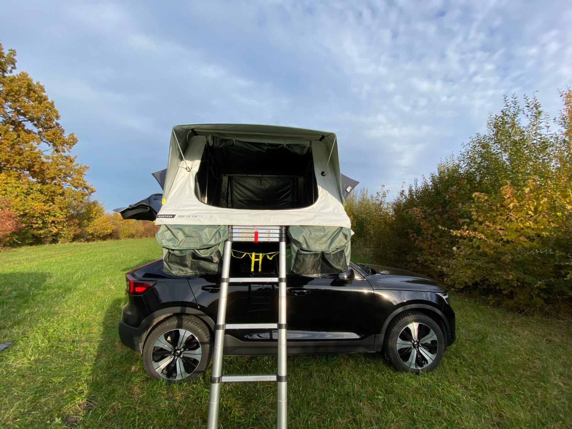 Dachzelt MH500 Schwarzes Auto mit einem aufklappbaren Dachzelt in einer Wiese.