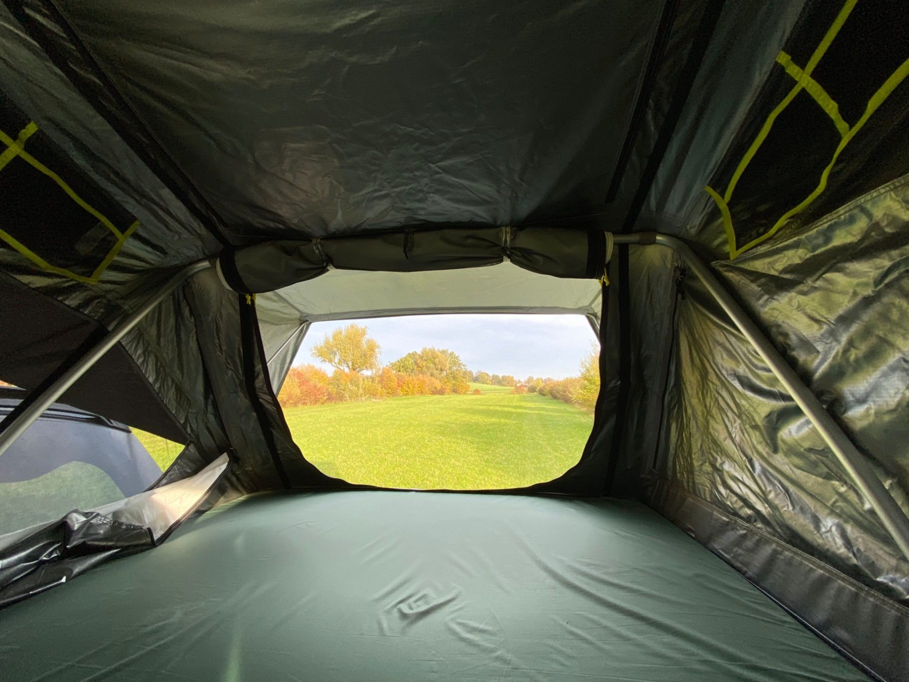Dachzelt innen Aussicht aus einem Zelt auf eine grüne Wiese mit herbstlichen Bäumen.