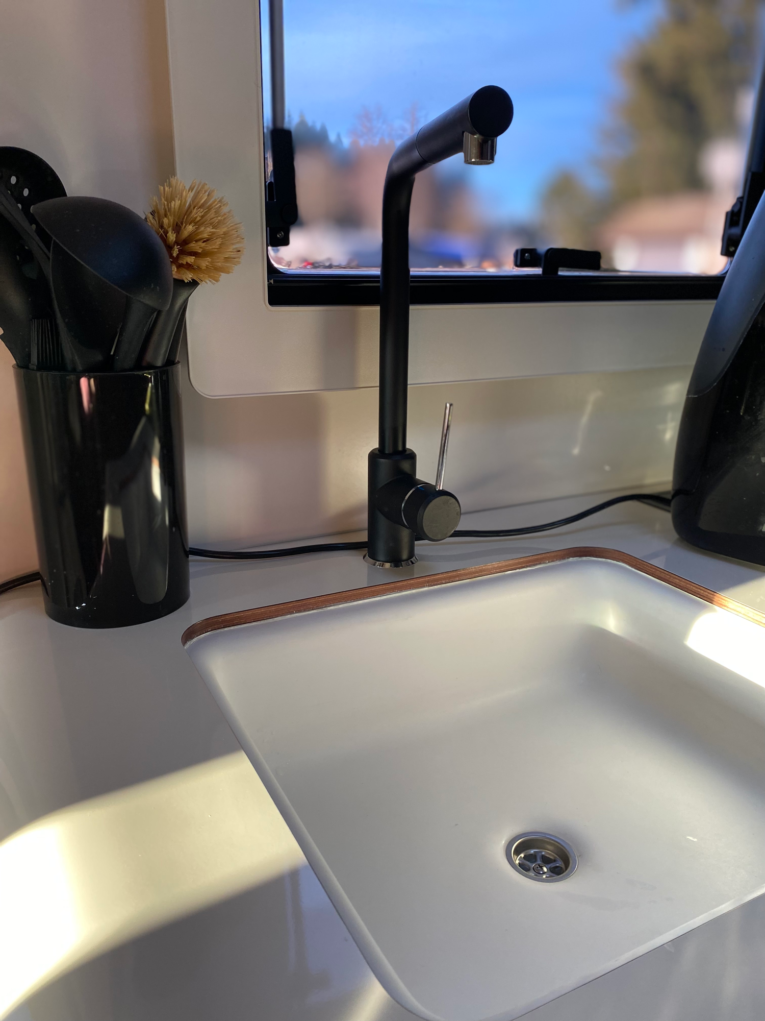 Großes Spülbecken Helle Küchenecke mit einem weißen Waschbecken und einem modernen schwarzen Wasserhahn.