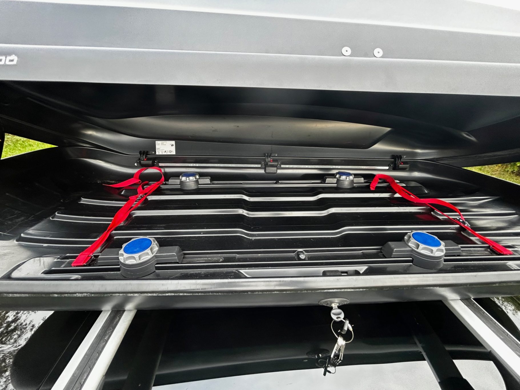 Dachbox von Innen Schwarzer Koffer mit roten Riemen und blauen Knöpfen, im Inneren mehrere Fächer.