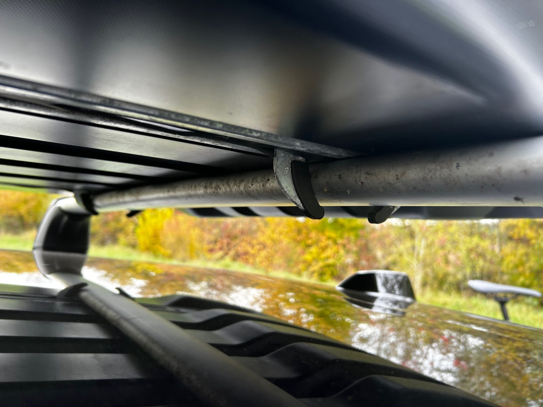 Befestigung auf Grundträger Blick unter einem Fahrzeugdach mit reflektierender Oberfläche und herbstlicher Landschaft.