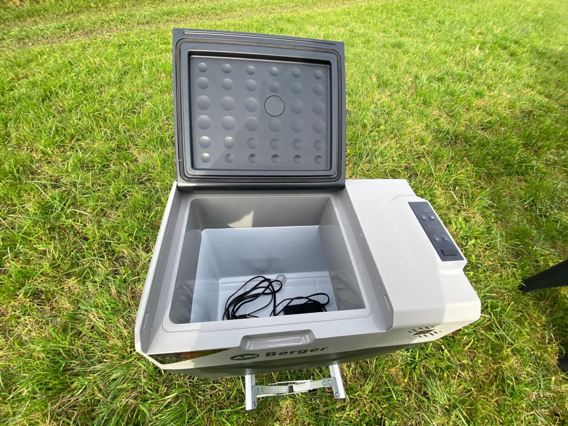 Platz für 1,5l Flaschen stehend Offene tragbare Kühlbox mit Kabel im Inneren, auf grüner Wiese platziert.