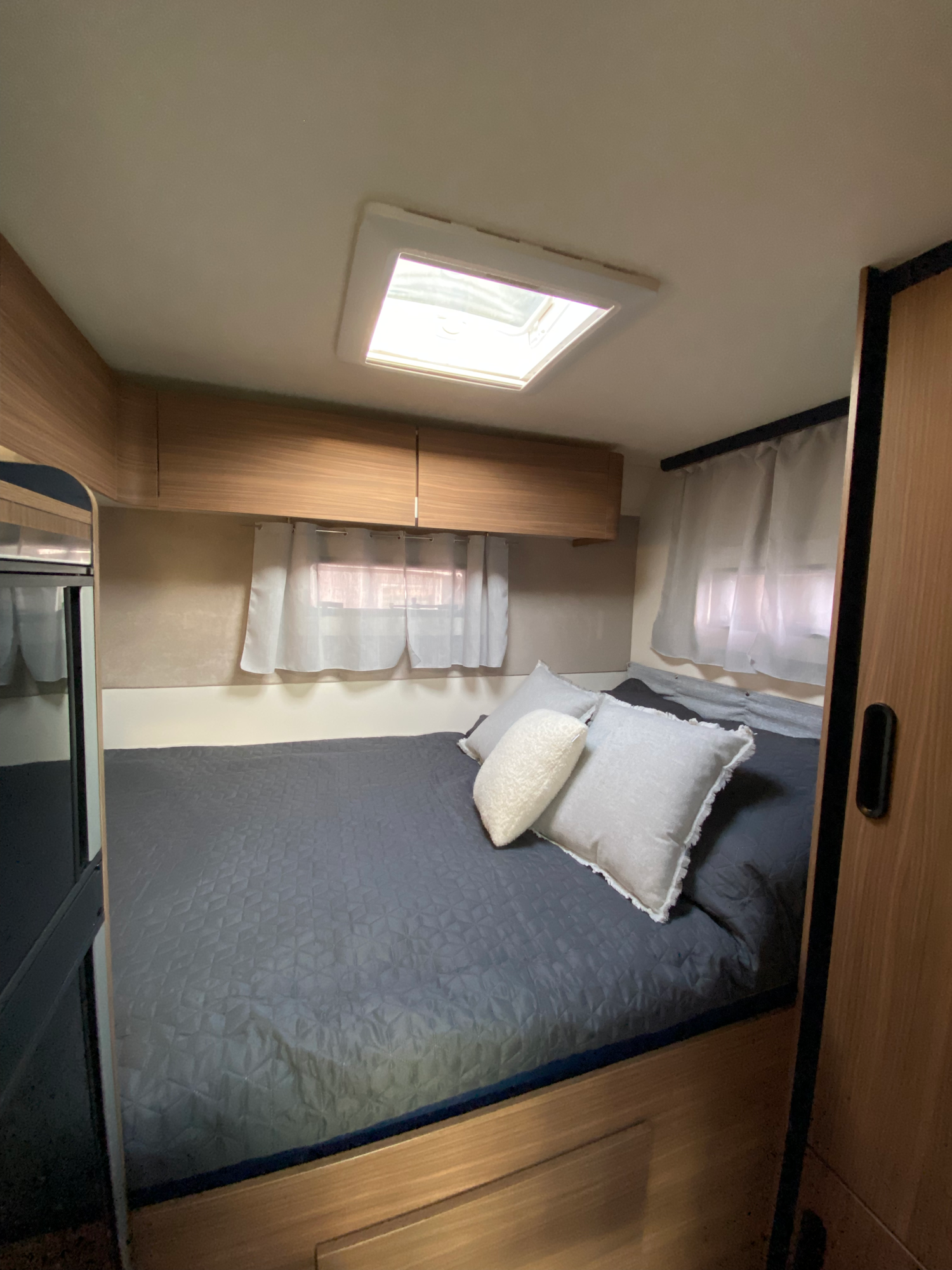 Unter dem Heckbett befindet sich eine Türe zur Heckgarage Gemütliches Schlafzimmer im Wohnmobil mit Bett, Kissen und Fenstern für Tageslicht.