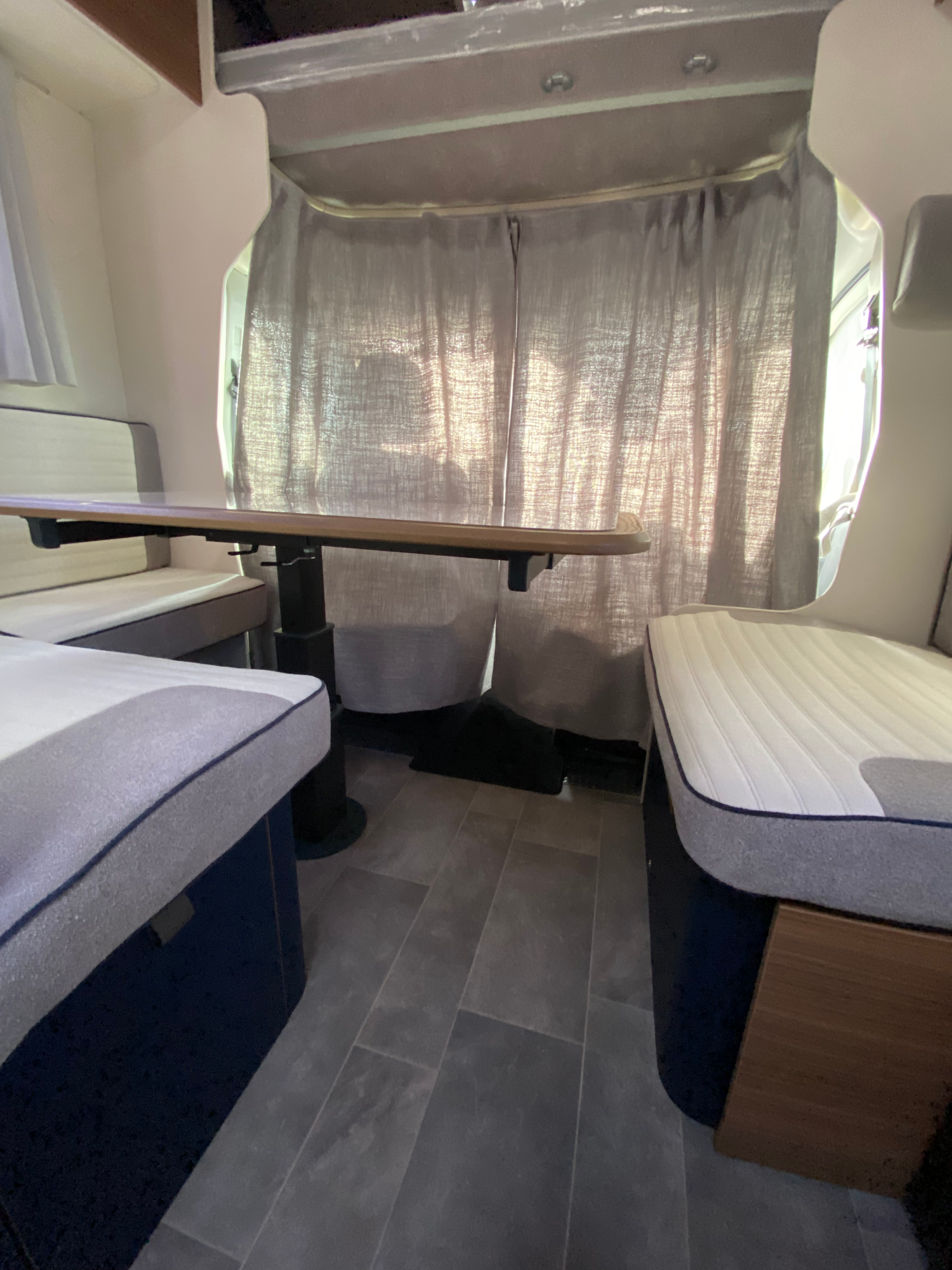 Die Vorhänge schaffen eine Abtrennung zum Cockpit Innenansicht eines Wohnmobils mit zwei Betten und einem Tisch in der Mitte.