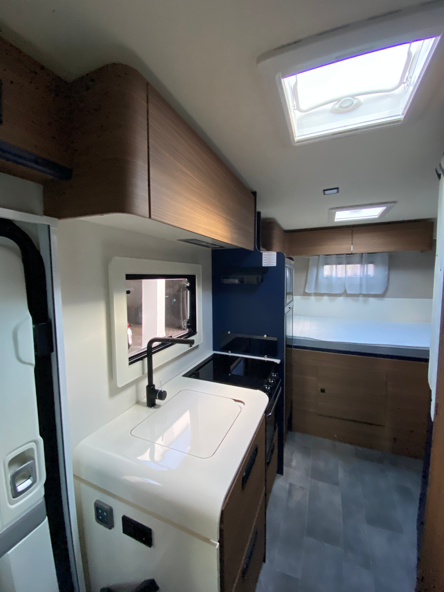 Blick auf die moderne & praktische Küche Moderne Wohnmobilküche mit Holzregalen, Spüle und Kochfeld, hell und offen gestaltet.