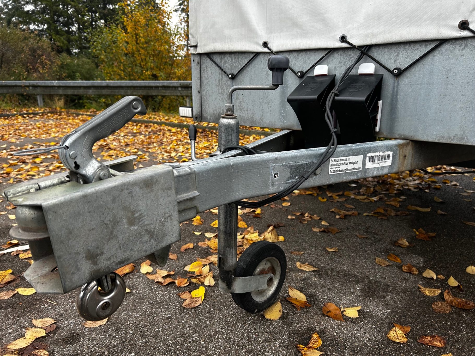 Stützrad, Keile & Deichselschloß Blick auf einen Anhängerkupplung mit Stützrad, umgeben von herbstlichen Blättern.