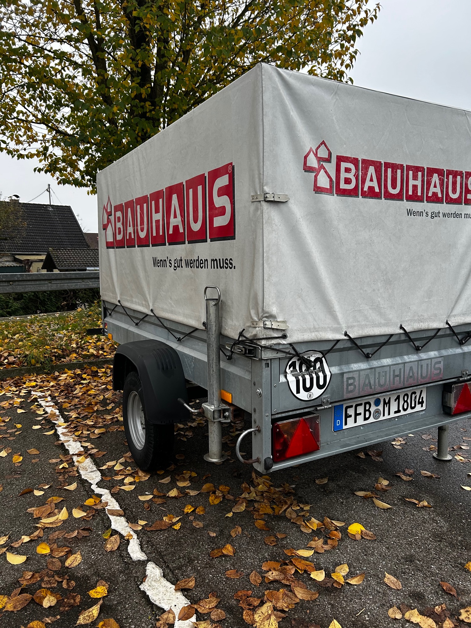 Anhänger mit 100km/h Zulassung Ein Anhänger mit BAUHAUS-Logo, parkt auf einer herbstlichen, laubbedeckten Straße.
