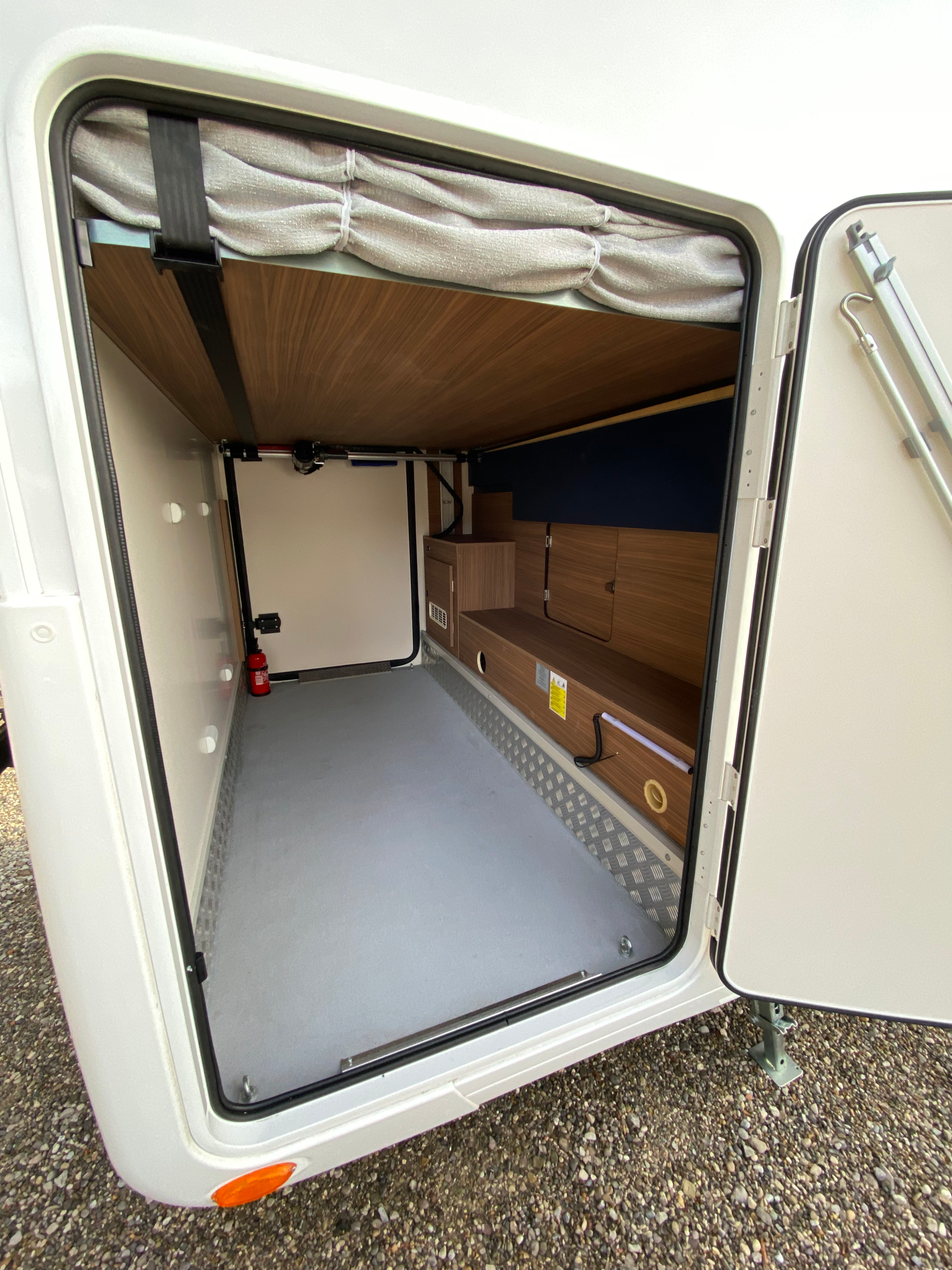 Die riesige Heckgarage mit dem höhenverstellbaren Heckbett Offene Tür eines Wohnmobils mit leerem Stauraum und Holzverkleidung.