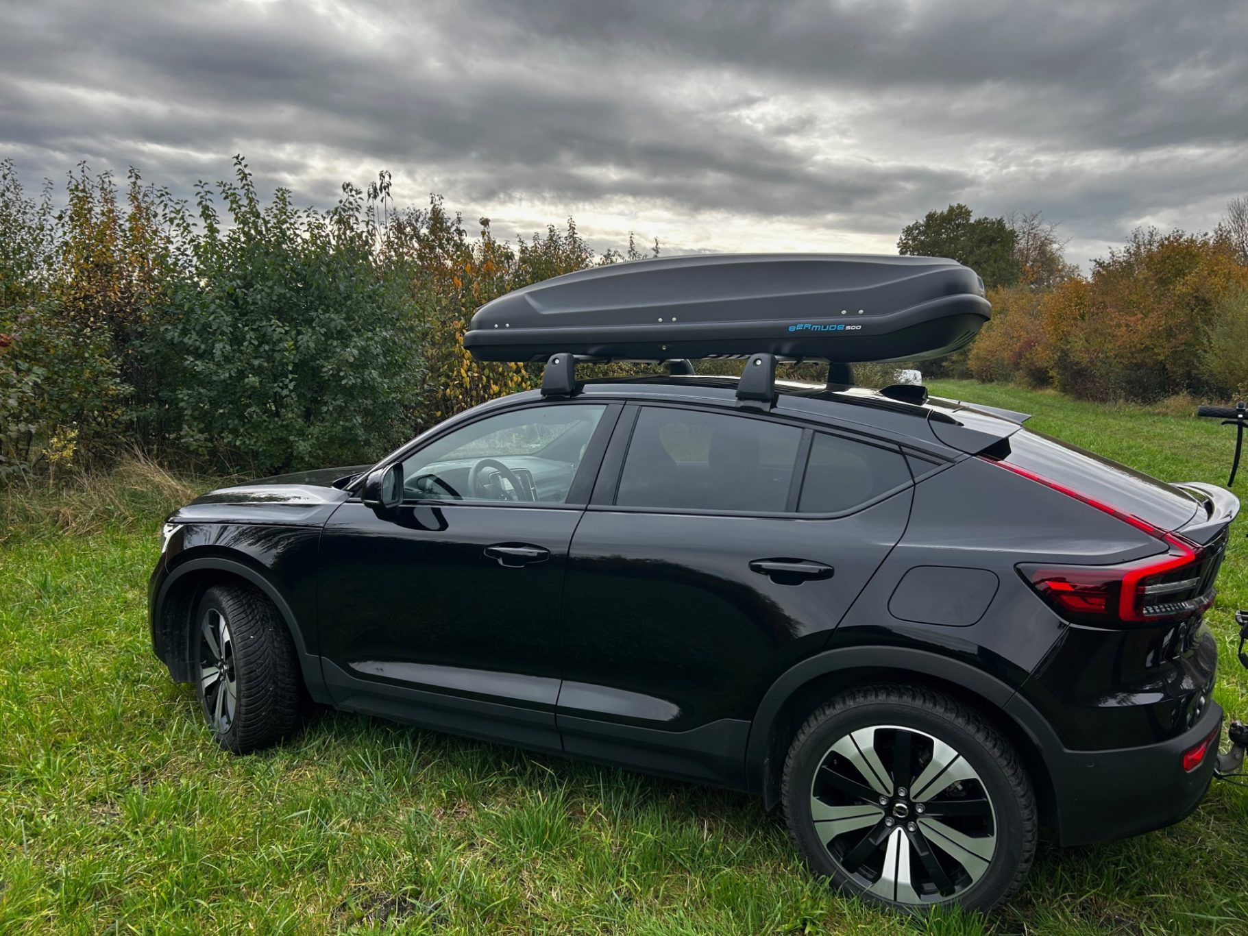 Dachbox Bermude 500 Schwarzer SUV mit Dachbox, parkt in einer grünen Wiese unter bewölktem Himmel.